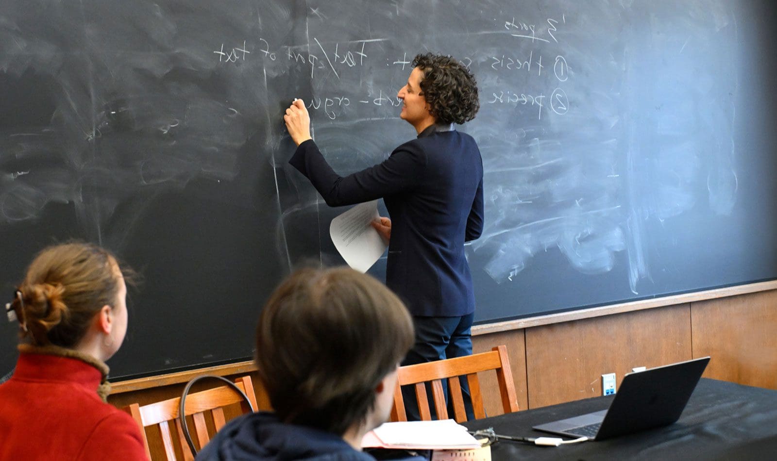 Faculty (Lisa Siraganian) writing on a chalkboard in front of a class.